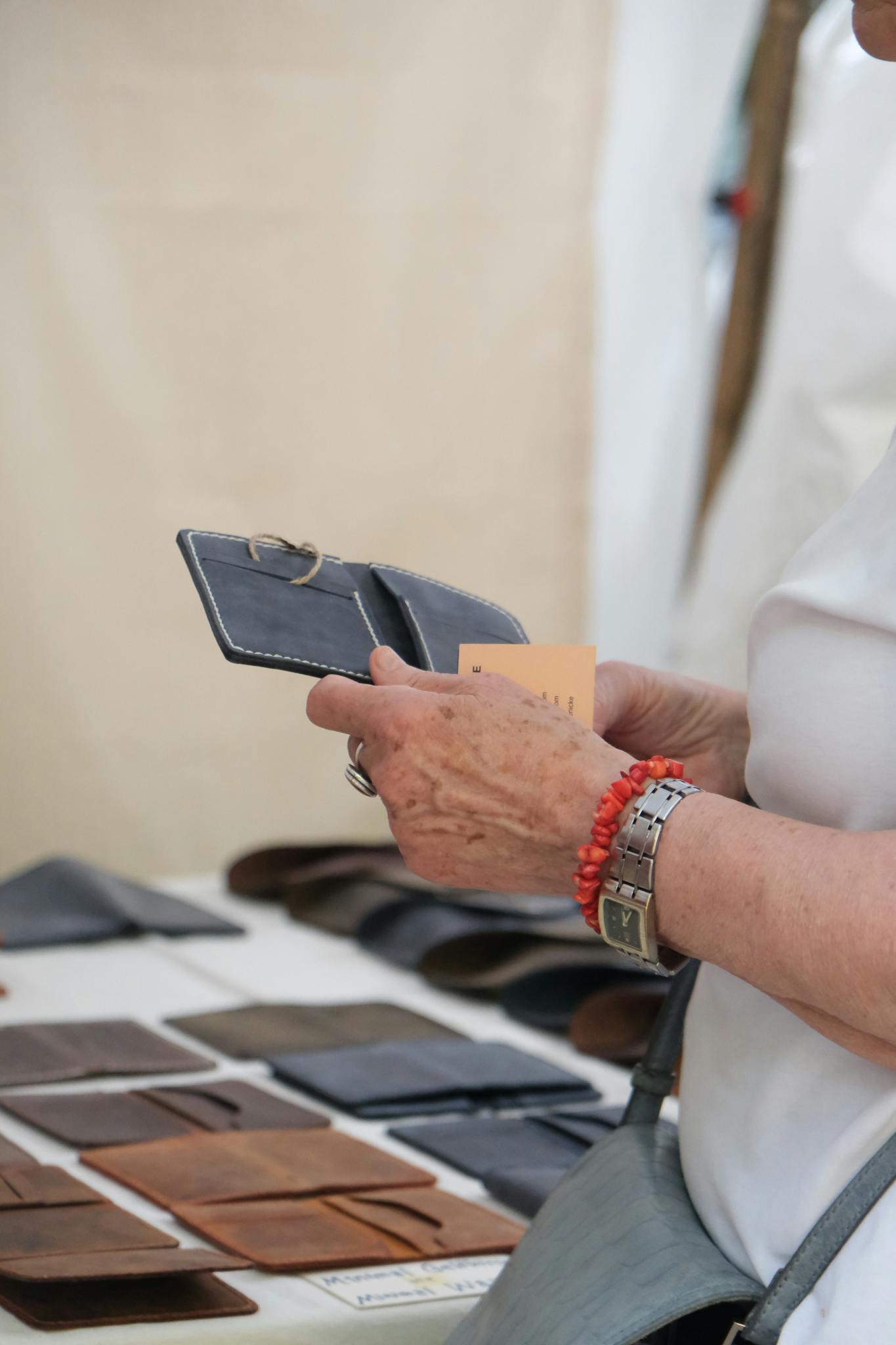 A person examines a leather wallet at an outdoor market, surrounded by other wallets on display.